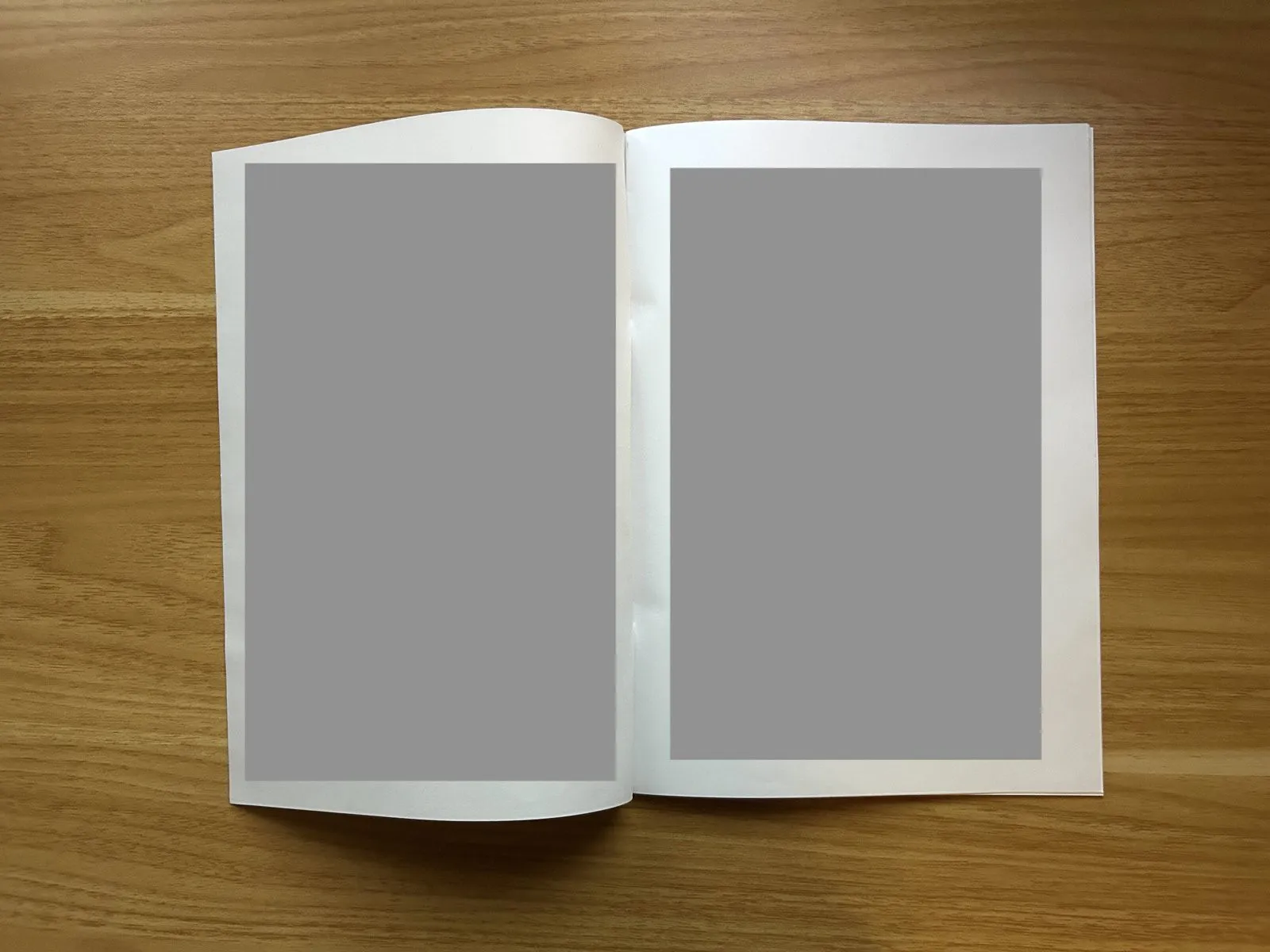 小冊子を見開きにしたところ。折り目をつけてあるので、ホッチキスの位置が真ん中でなくても平らに開いている。中身は灰色で塗りつぶし